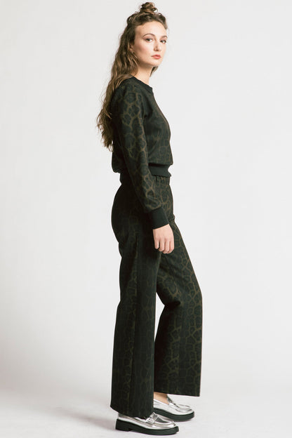 Side view of a woman wearing the Gone Top by Allison Wonderland in Leopard, a classic crewneck, with matching pants. She is standing in front of a white background. 