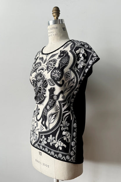 Side view of the Malo T-shirt from Kollontai, featuring a floral and panther print in black-on-ivory on the front, cap sleeves, and a solid black back, shown on a mannequin in front of a grey background 