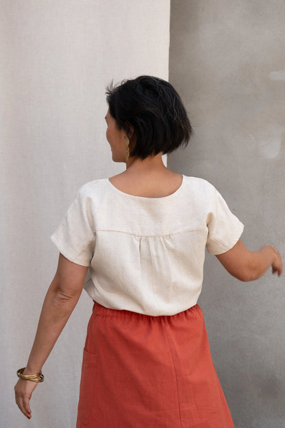 Back view of a woman wearing the Nymphea Screenprinted Skirt by Kazak in Red Pysanka with a cream top, she is standing outside in front of white curtain. 