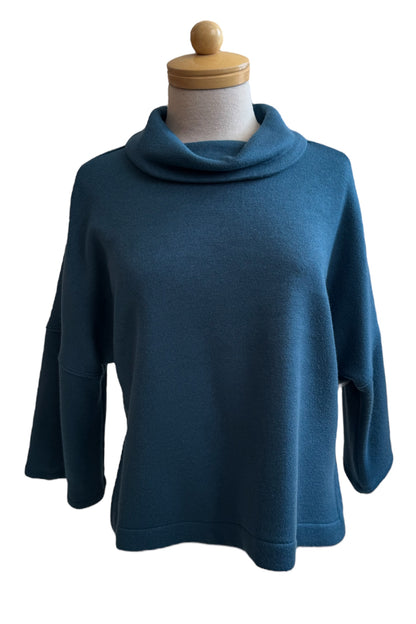 The Paige Sweater by Compli K in Peacock, featuring a large cowl neck, drop-sleeves, a loose fit, and side slits, is shown on a mannequin against a white background. 