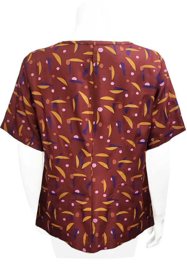 A back view of the Cecil Box Blouse by Mandala in Playtime Rust print is shown on a mannequin against a white background. It has a high neckline, wide 1/2 sleeves, and a side hem slit detail.