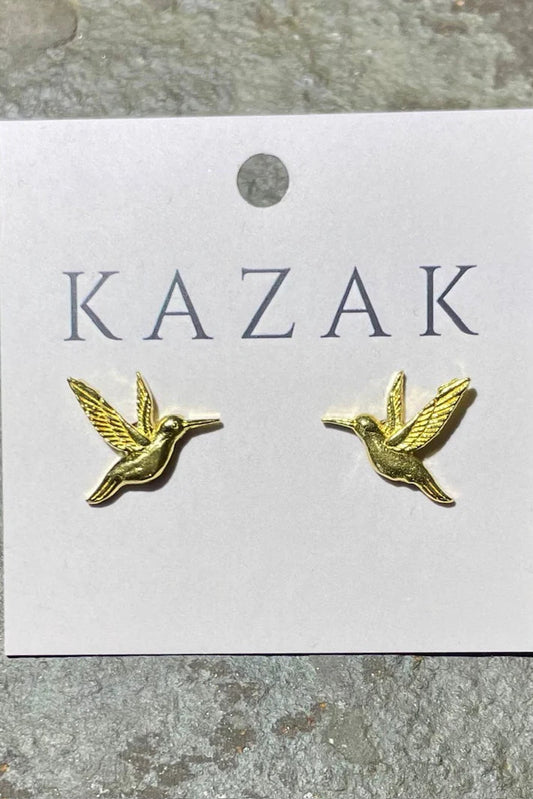 Brass hummingbird earrings on a 'KAZAK' branded card against a textured grey background