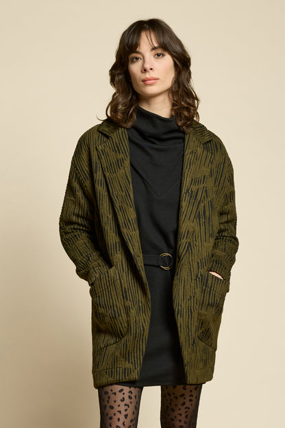 A woman wearing the Call Me Jacket by Cokluch in Olive, a thigh-length open collared jacket in unique Crinkle Max fabric with two large patch pockets. She is wearing it over a black outfit on a beige background.