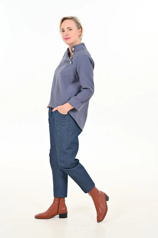 Side view of a woman wearing the Alice Cocoon Pants by Julei Design in Denim with a blue top, standing in front of a white background 