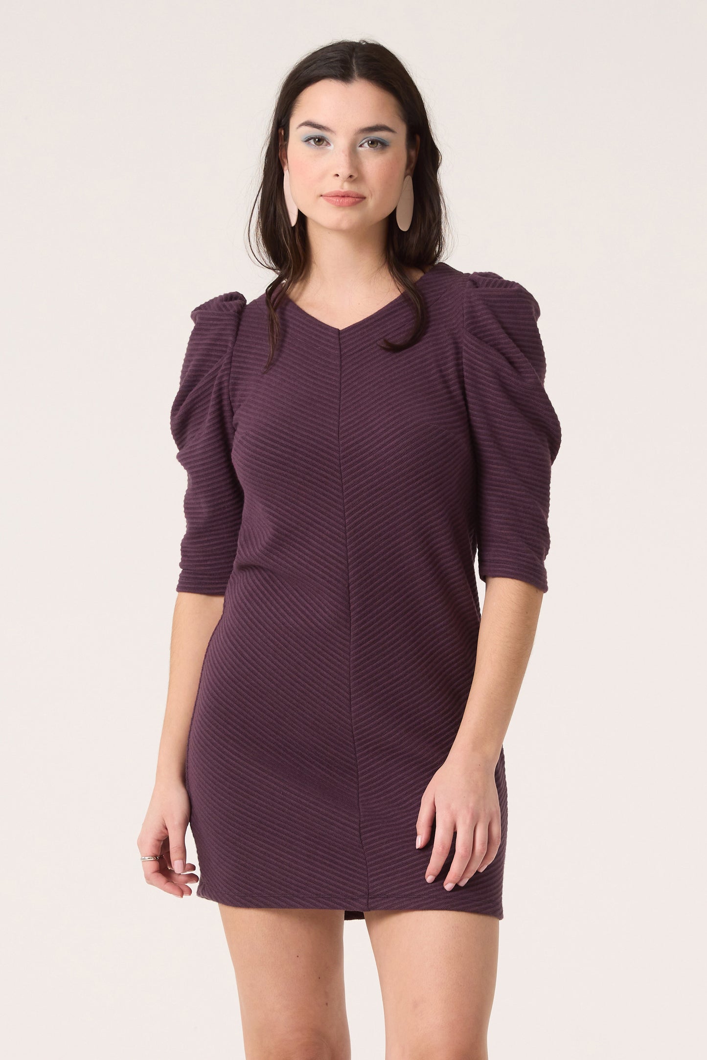 3/4 shot of a woman wearing the Celeste Dress by Cokluch in Blackberry, standing in front of a white background