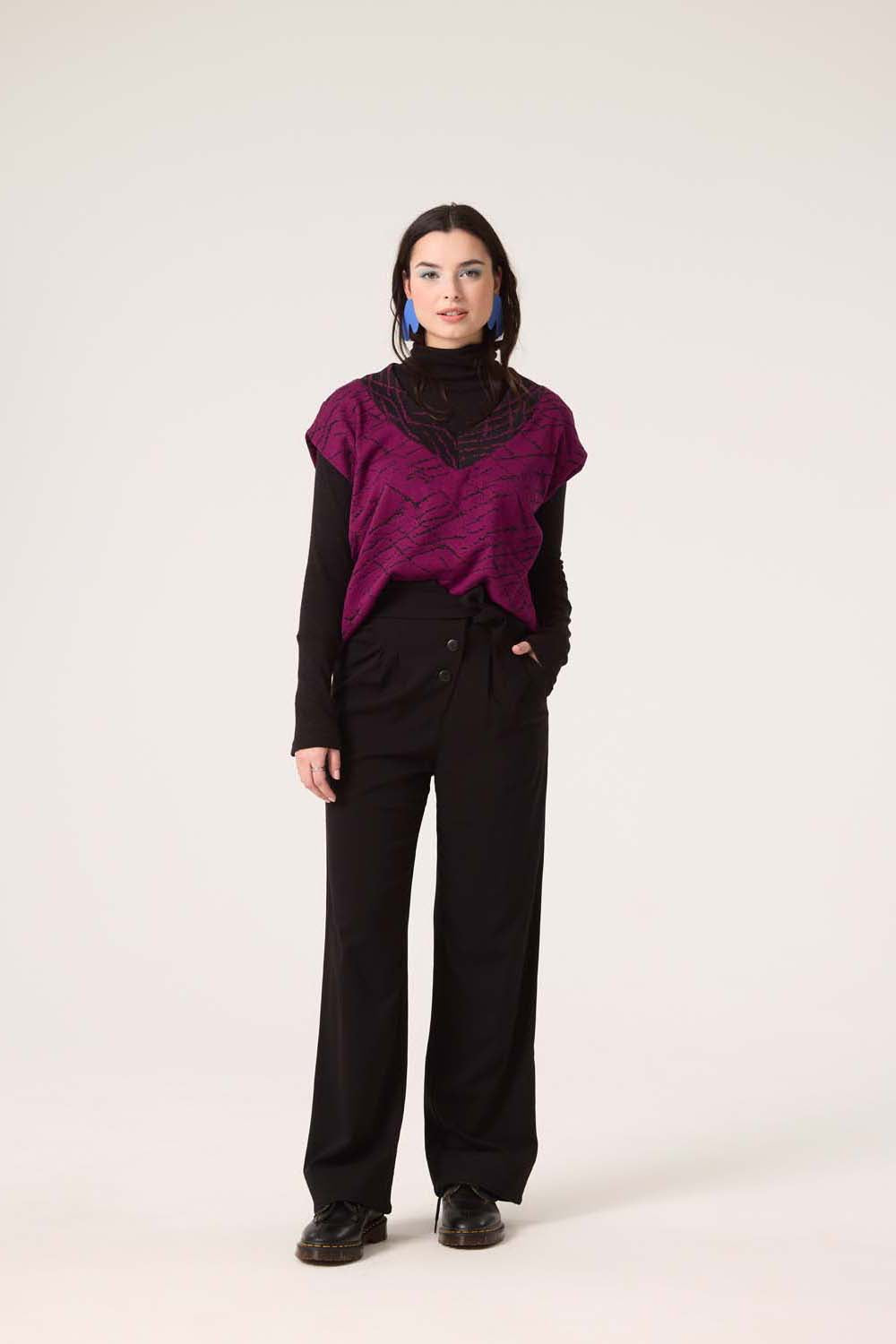 A woman wearing the Centaur Top by Cokluch in Magenta with Black pants, standing in front of a white background 