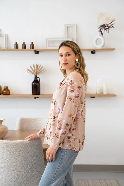 Side view of a woman wearing the Martini Blouse by Cherry Bobin in pale pink Floral, a button front shirt with a classic collar. She is wearing it with light blue jeans and standing by a table. 