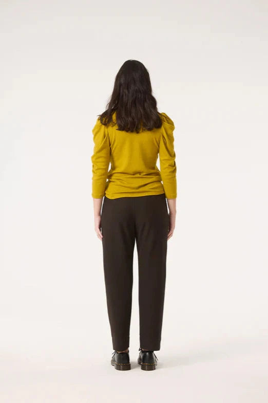 Back view of a woman wearing the Nenuphar Top by Cokluch in Avocado, featuring a high collar and 3/4 length puffed sleeves, with the Belief Pants in Pine. She's standing in front of a white background. 