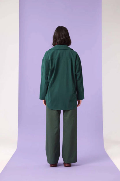 Back view of a woman wearing the Willow Top by Cokluch in Eden, standing in front of a purple background 