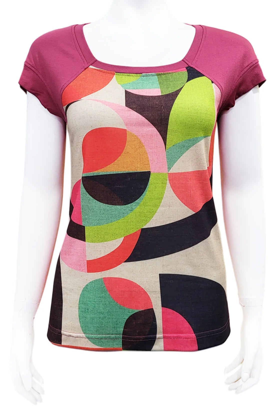 The Decades Era Tee by Mandala in 50s Mod, featuring a geometric print with pink sleeves, is shown on a mannequin in front of a white background. 