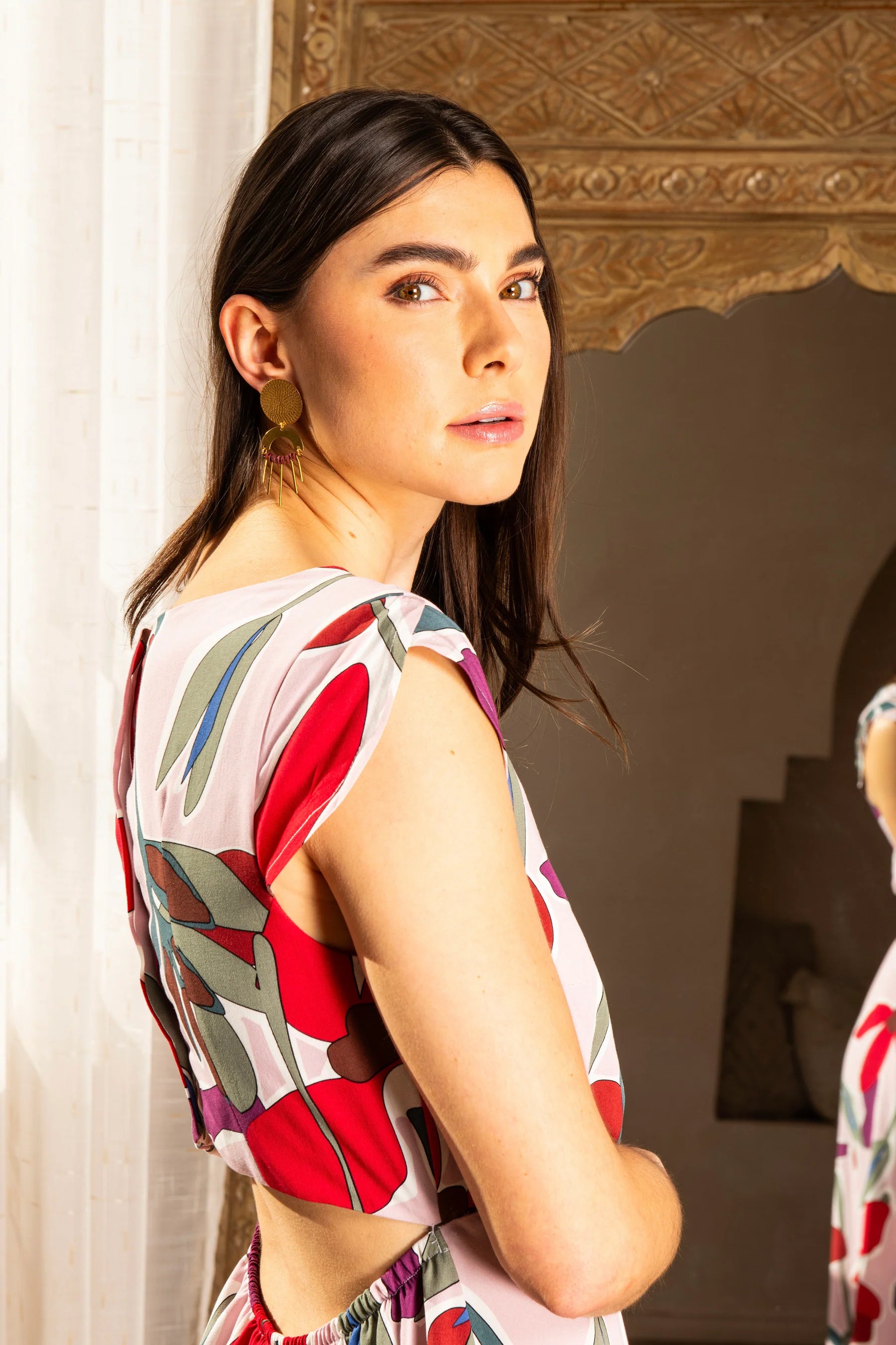 Side view close-up photo of a woman wearing the Maree Dress by Cherry Bobin, featuring a pink floral pattern, standing in front of a mirror