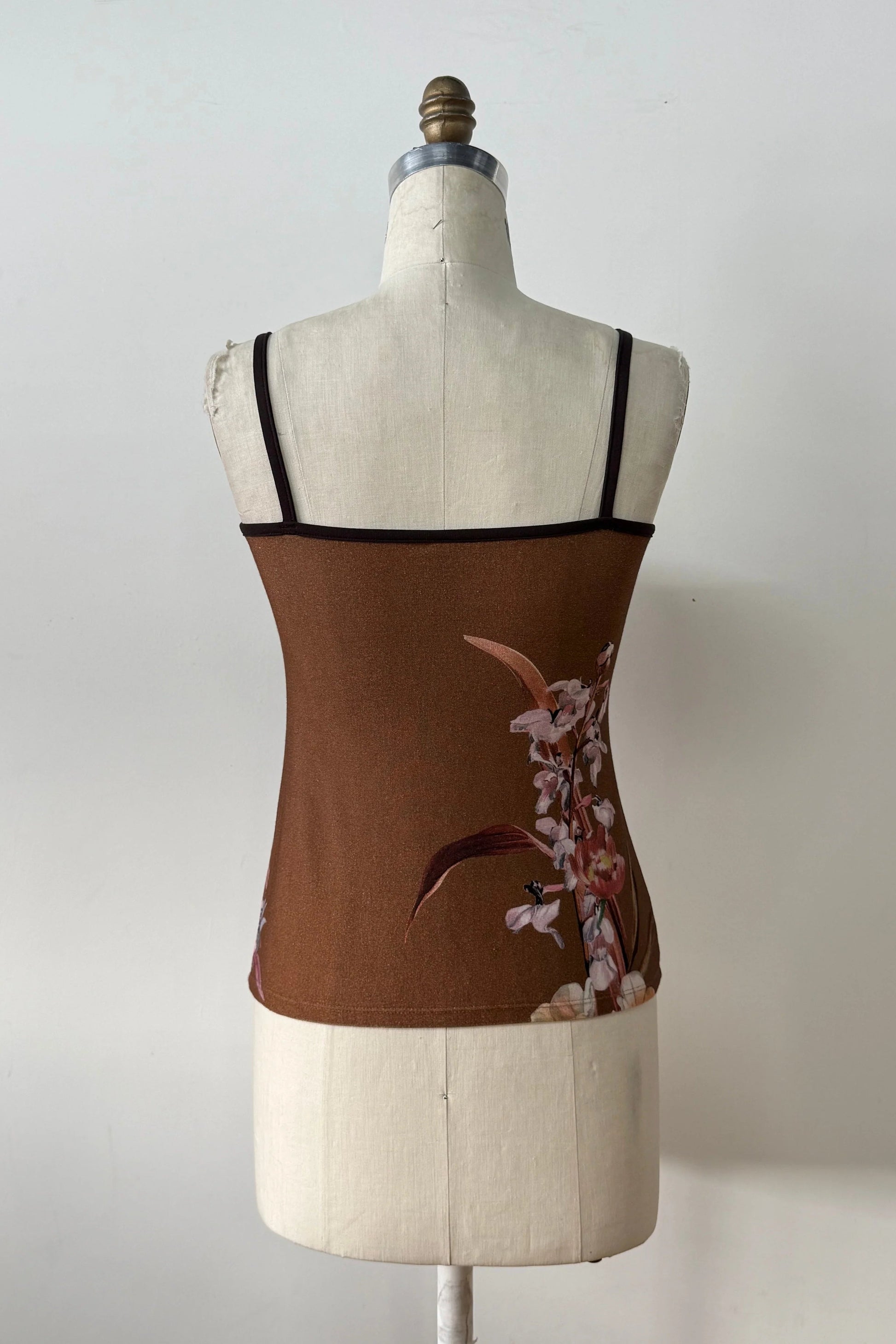 A back view of the Morganne Top by Kollontai, a brown floral tank top with spaghetti straps, is shown on a mannequin against a grey background