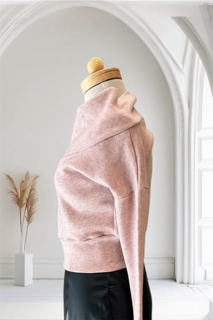 A side view of the Changes Sweater by Allison Wonderland in Pink, featuring a large cowl neck, long dropped sleeves, and a wide waistband, is shown with the Desire Skirt in Black against a white arched backdrop. 