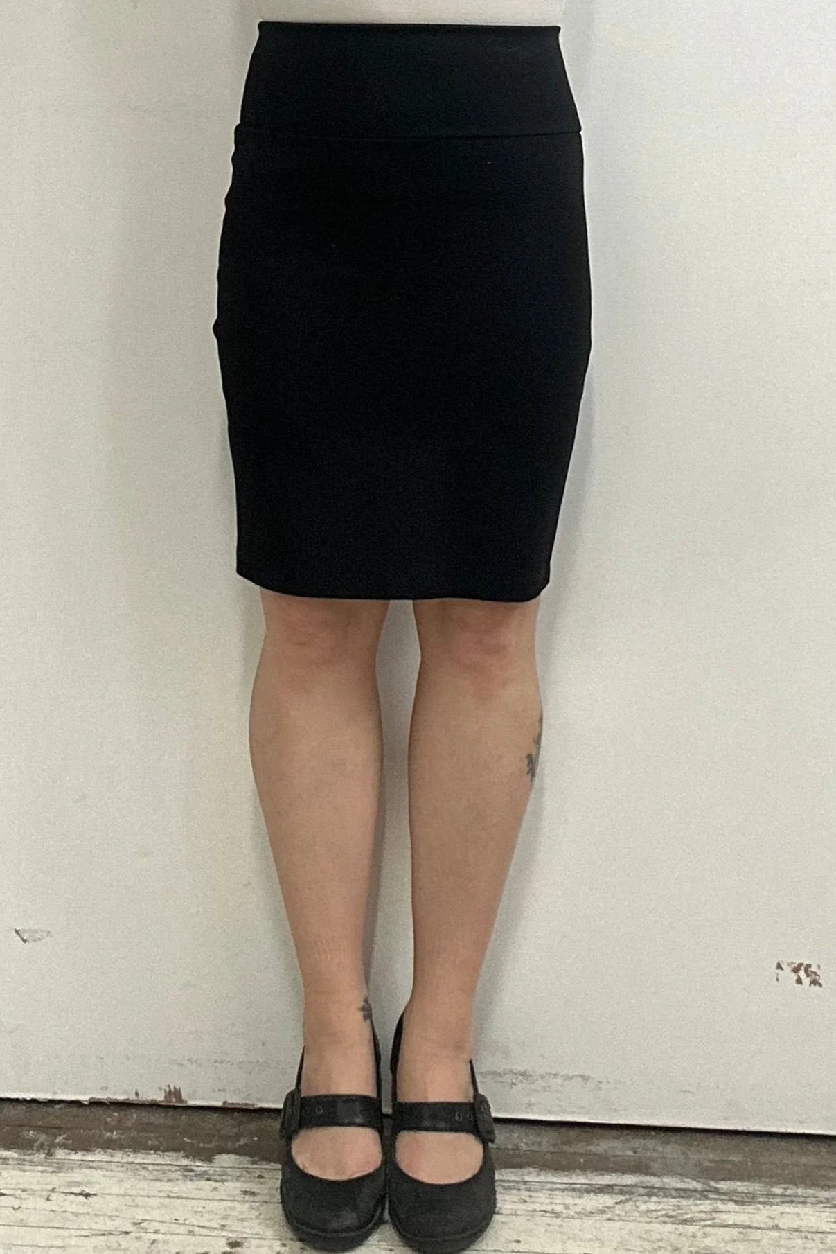 Waist down view of a woman wearing the Veneto Skirt by Kollontai in Black, a pencil skirt with a wide-pull on waistband that hits above the knee.