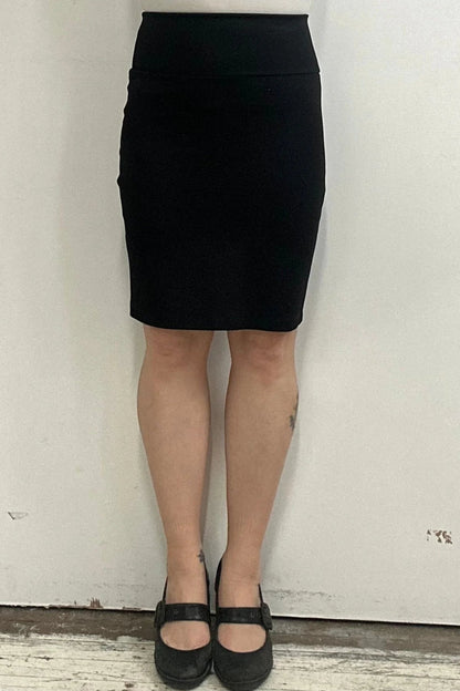 Waist down view of a woman wearing the Veneto Skirt by Kollontai in Black, a pencil skirt with a wide-pull on waistband that hits above the knee.
