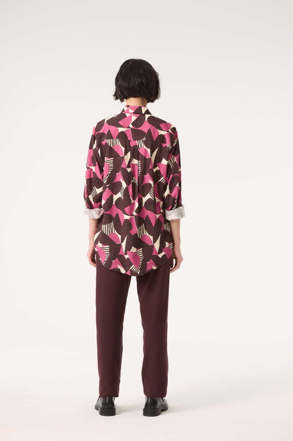 Back view of a woman wearing the Frontiers Shirt by Cokluch in Berry Half Moon print with the Belief Pants in Shiraz, standing in front of a white background 