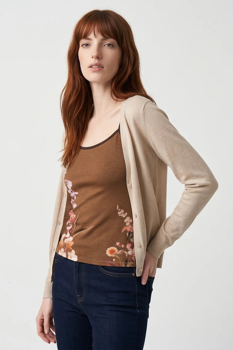 A woman wearing the Morganne Top by Kollontai, a brown floral tank top with spaghetti straps. She is wearing it with blue jeans and a cream cardigan against a white background