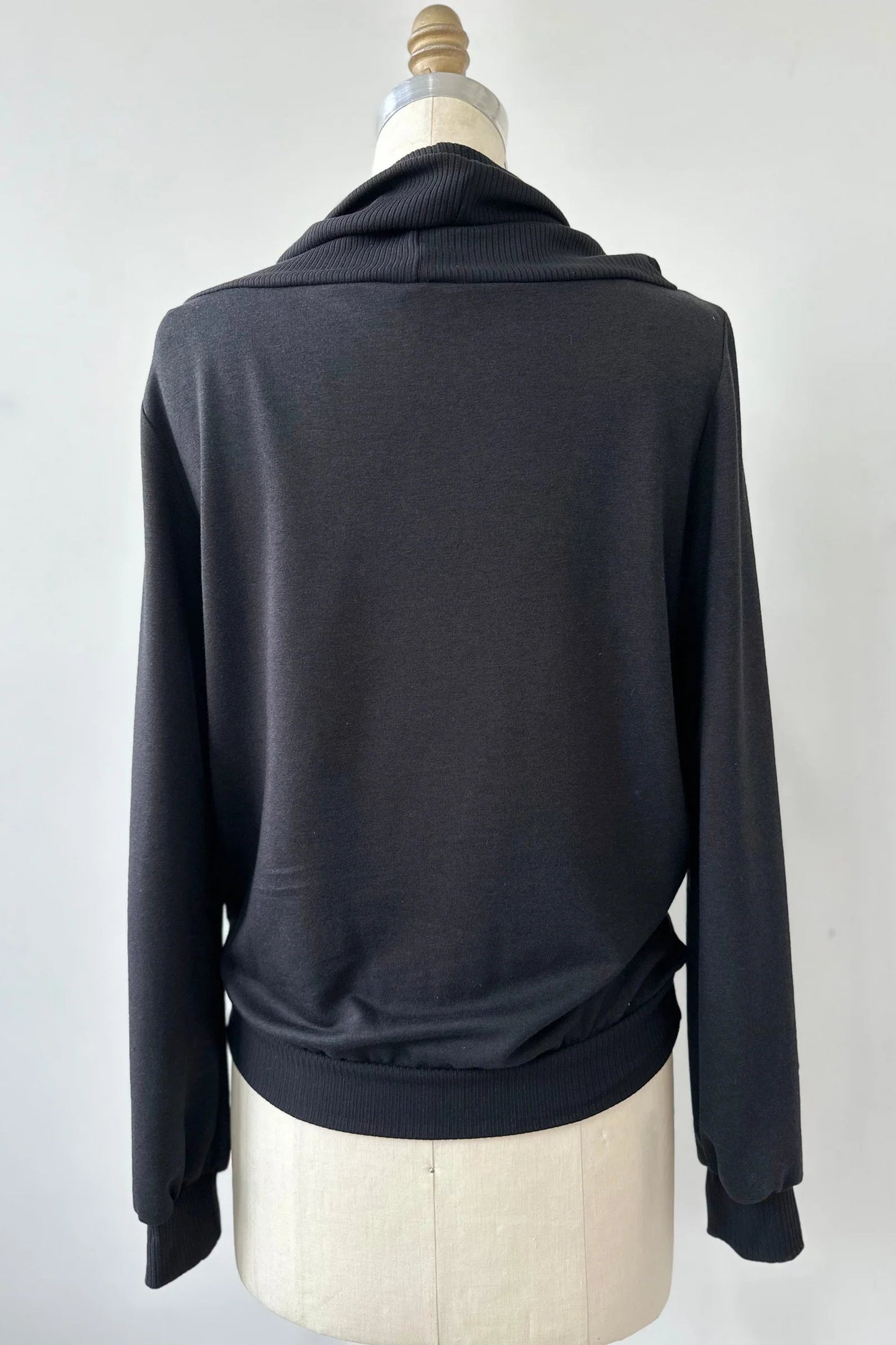 A back view of the Jullian Sweater by Kollontai in Black, with a cowl neck, long sleeves, and a kangaroo pocket, is shown on a mannequin in front of a white background. 