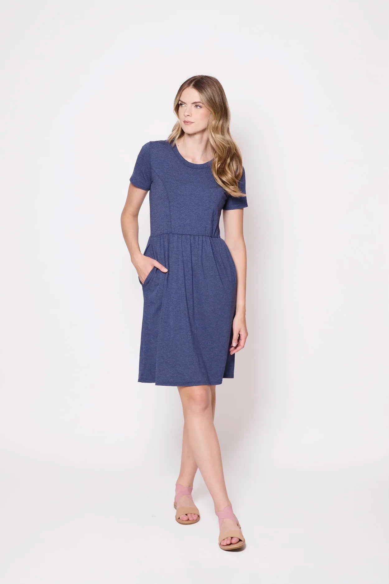 A woman wearing the Hayley Dress by Tangente in Heather Lake, a short sleeved bamboo dress with a gathered knee-length skirt. She is standing outside in front of a white background.