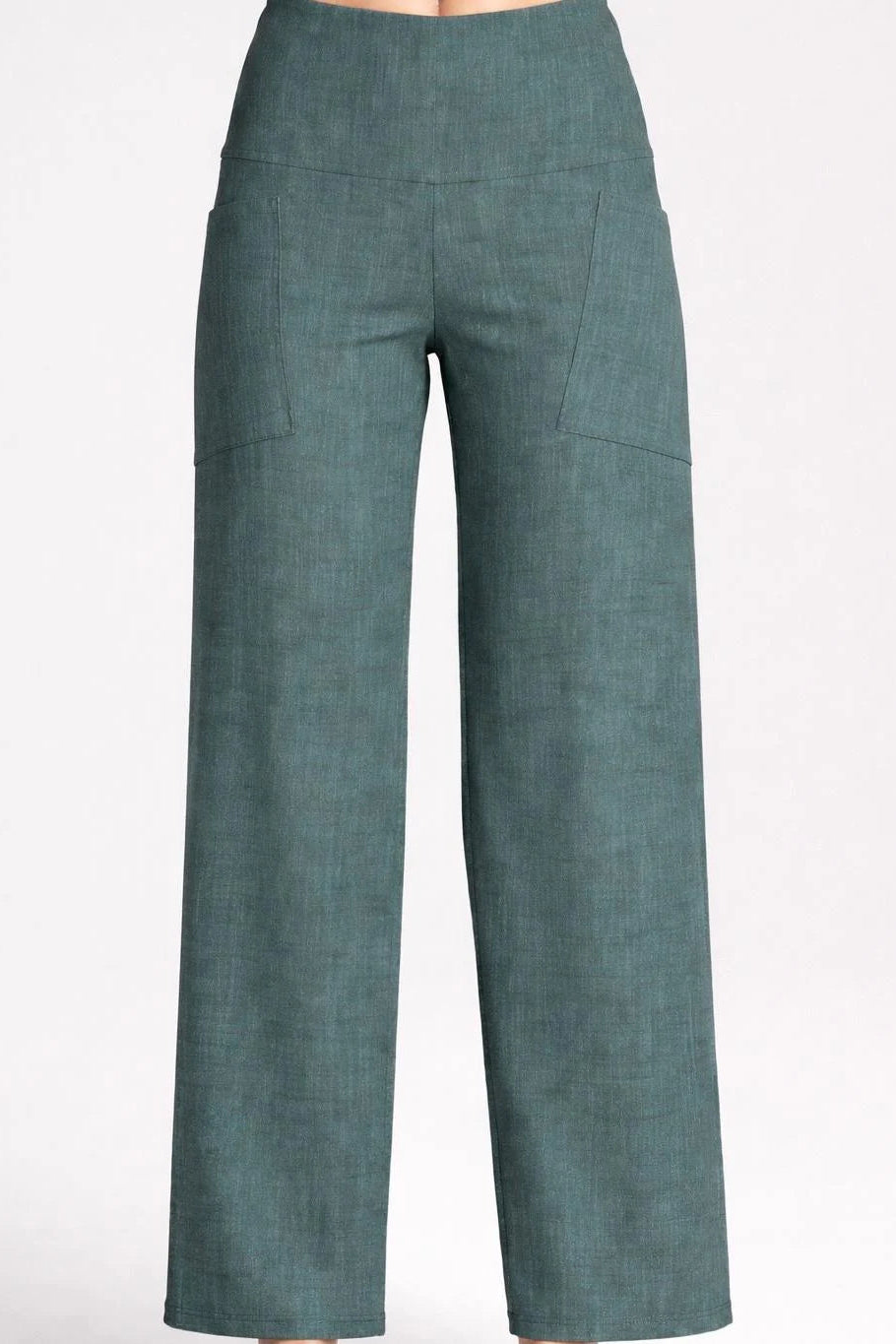 Waist down view of a woman wearing the Kollontai Susan Pants in Green, standing in front of a grey background. 