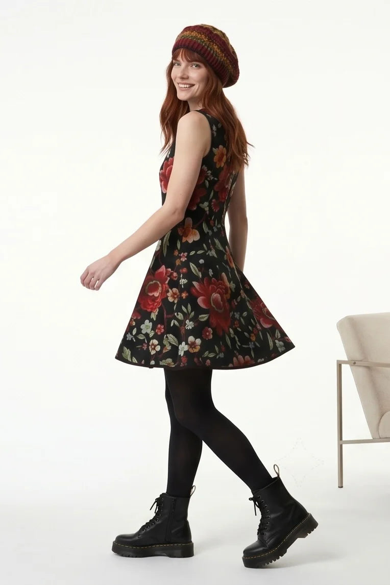 Side view of a  woman wearing the Silba Dress FW26/27 by Kollontai in Black Floral, a short sleeveless dress with princess seams and an above the knee skirt. She is standing against a white background. 