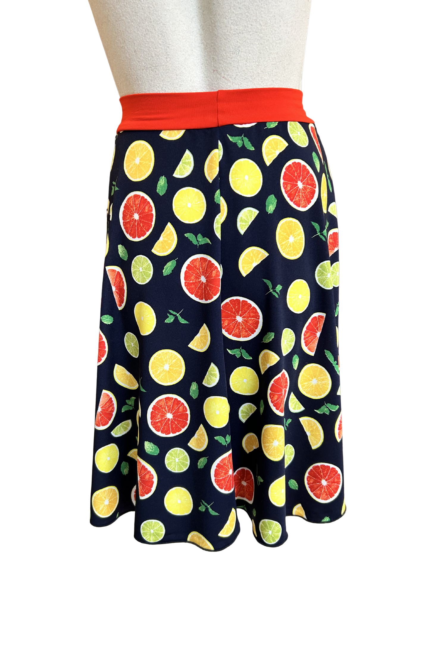 A back view of the Flirt Skirt by Slak in Citrus Print, an above the knee A-line skirt with a contrasting pull-on waistband, is shown on a mannequin against a white background. 