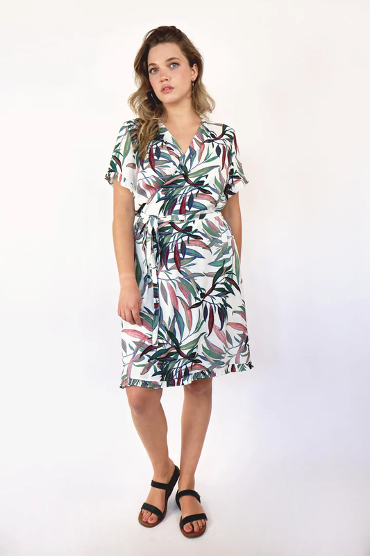 A woman wearing the Atlas Wrap Dress by Korelli, in a Tropical print and rayon fabric, standing in front of a white background