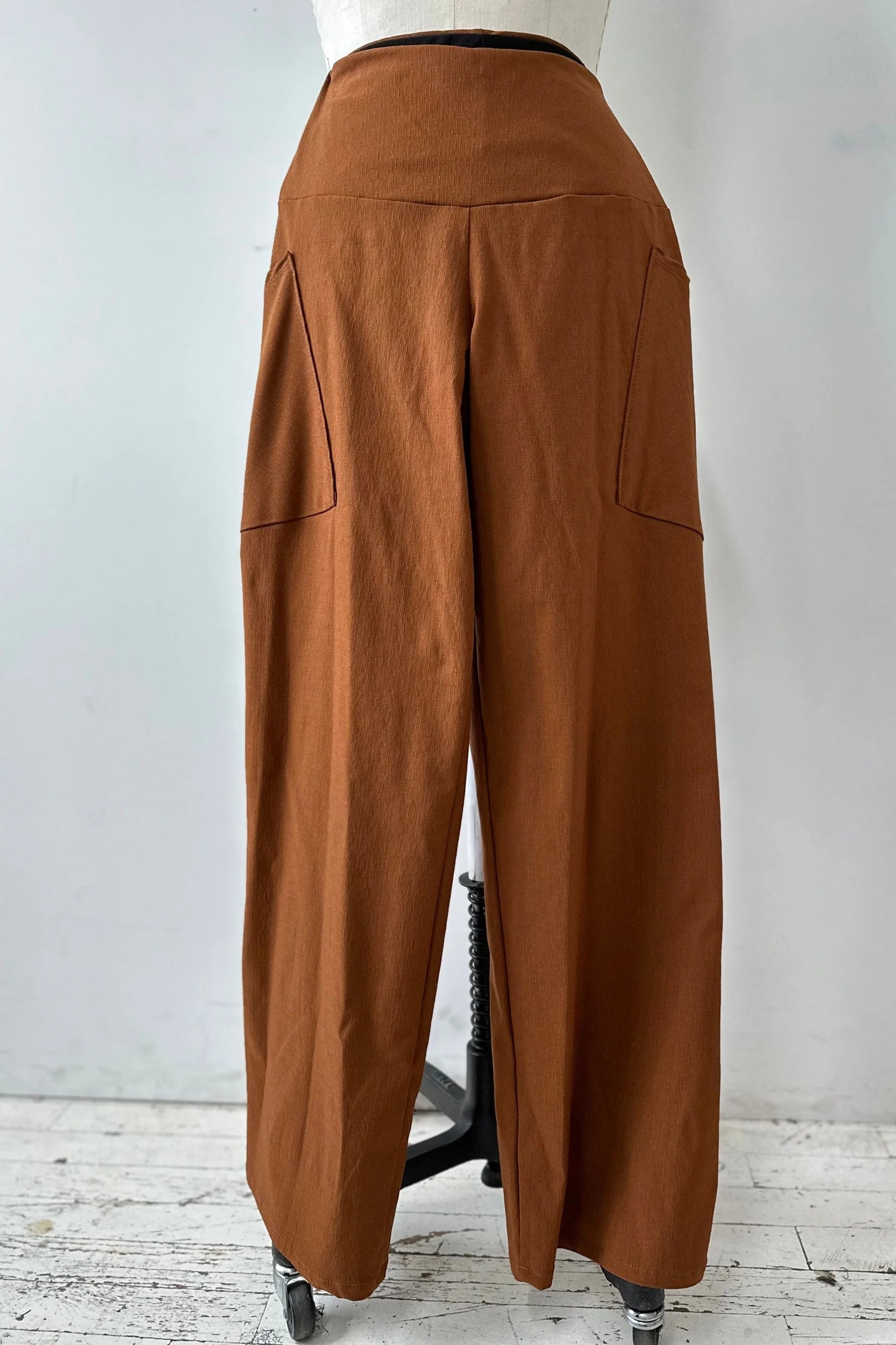 The Frydek Pants by Kollontai in Cinnamon, featuring wide legs, a wide pull-on waistband, and angled patch pockets, are shown on a mannequin in front of a white background. 