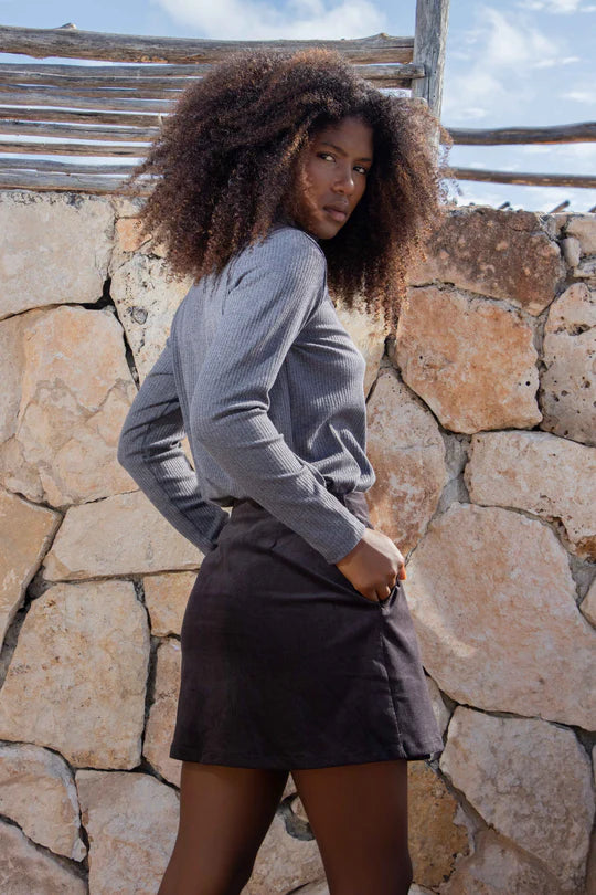 Side view of a woman wearing the Tucson Top by MAS in Iron with a dark skirt, standing outside in front of a rocky wall 