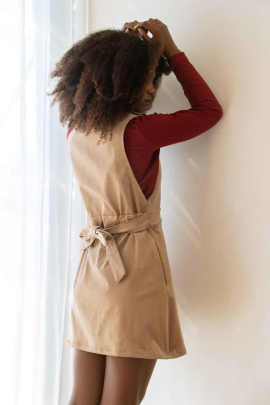 Back view 3/4 shot of a woman wearing the Tucson Top by MAS in Ruby with beige jumper, standing in front of  white curtain and wall  