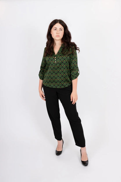 A women wearing the Leonie Blouse by Infime in Black with Green print, featuring a notched V-neckline, three button placket, and 3/4 sleeves. She is wearing it with black pants and standing in front of a white background. 