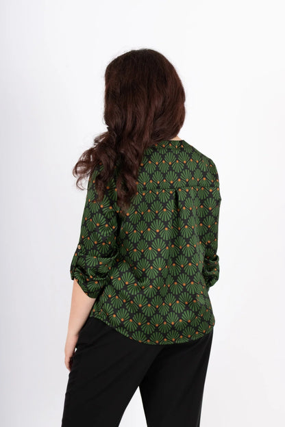 Back view of a woman wearing the Leonie Blouse by Infime in Black with Green print, featuring a notched V-neckline, three button placket, and 3/4 sleeves. She is wearing it with black pants and standing in front of a white background. 