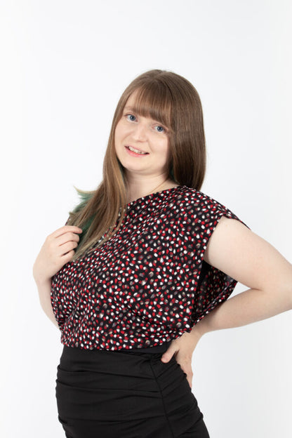 A woman wearing the Saki Top by Infime in Red brushstrokes with a black skirt, standing in front of a white background 