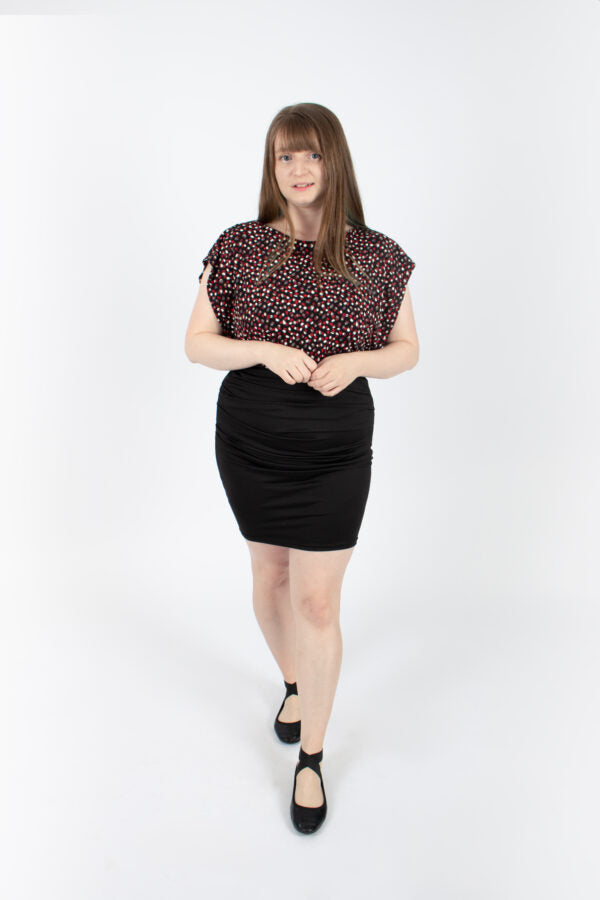 A woman wearing the Saki Top by Infime in Red brushstrokes with a black skirt, standing in front of a white background 