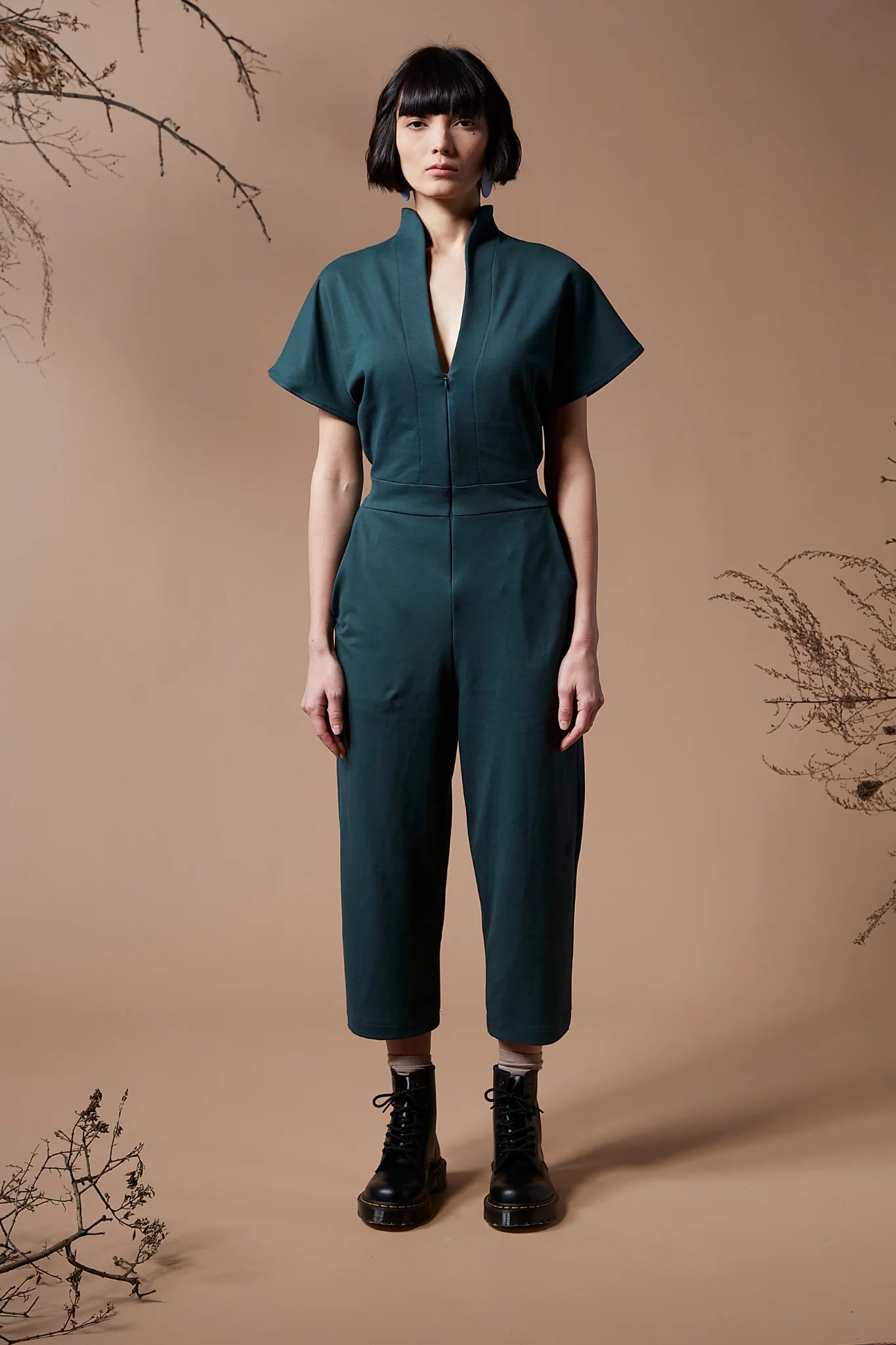 a woman wearing the Jayden Jumpsuit by Melow in Forest, standing in front of a beige background