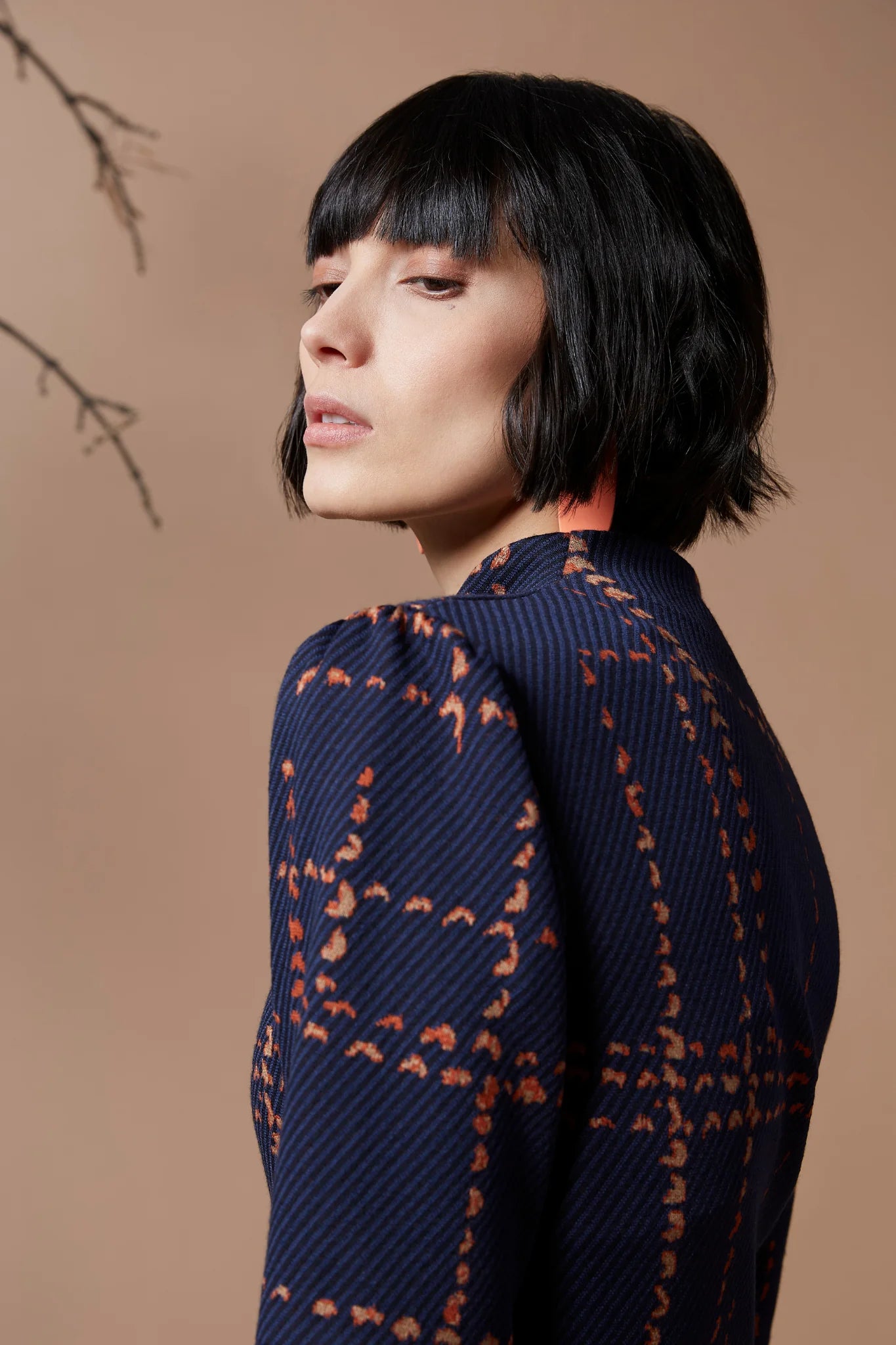 Close up side view of a woman wearing the Jonathan Jumpsuit by Melow in Indigo, standing in front of a beige background