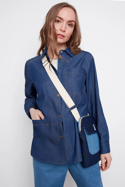 A woman wearing the Jasmine Denim Shirt by Julei, a boyfriend style button front shirt with a chest pocket and a large front patch pocket. She is wearing it with jeans and standing in front of a white background. 