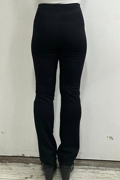Back waist down view of a woman wearing the Bari Pants by Kollontai, black pants with a slim fit, wide pull-on waistband, and front patch pockets, in front of a white wall. 