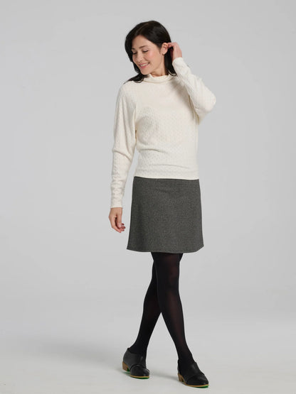 A woman wearing the Frost Skirt by Kollontai in Charcoal tweed, an above the knee length A-line skirt with an elastic waist.  She is wearing it with a black top and standing in front of a grey background. 