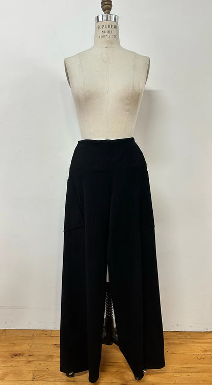 The Hermione Pants by Kollontai in Navy, stretchy corduroy pants with a wide pull-one waistband, wide legs, and angled patch pockets, are shown on a mannequin in front of a white wall. 