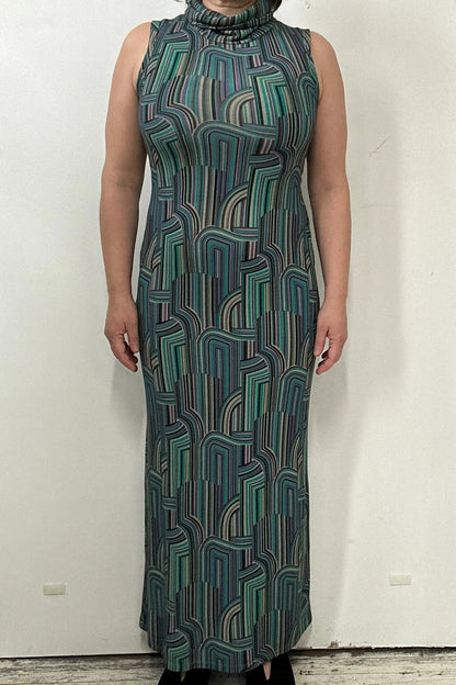 A woman wearing the Ysia Dress by Kollontai, a sleeveless turtleneck dress with a geometric pattern. She is standing in front of a white background. 