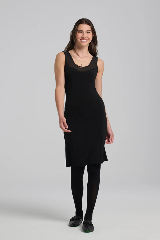 A woman wearing the Shelley Dress by Kollontai in Black, with  black tights, standing in front of a white background