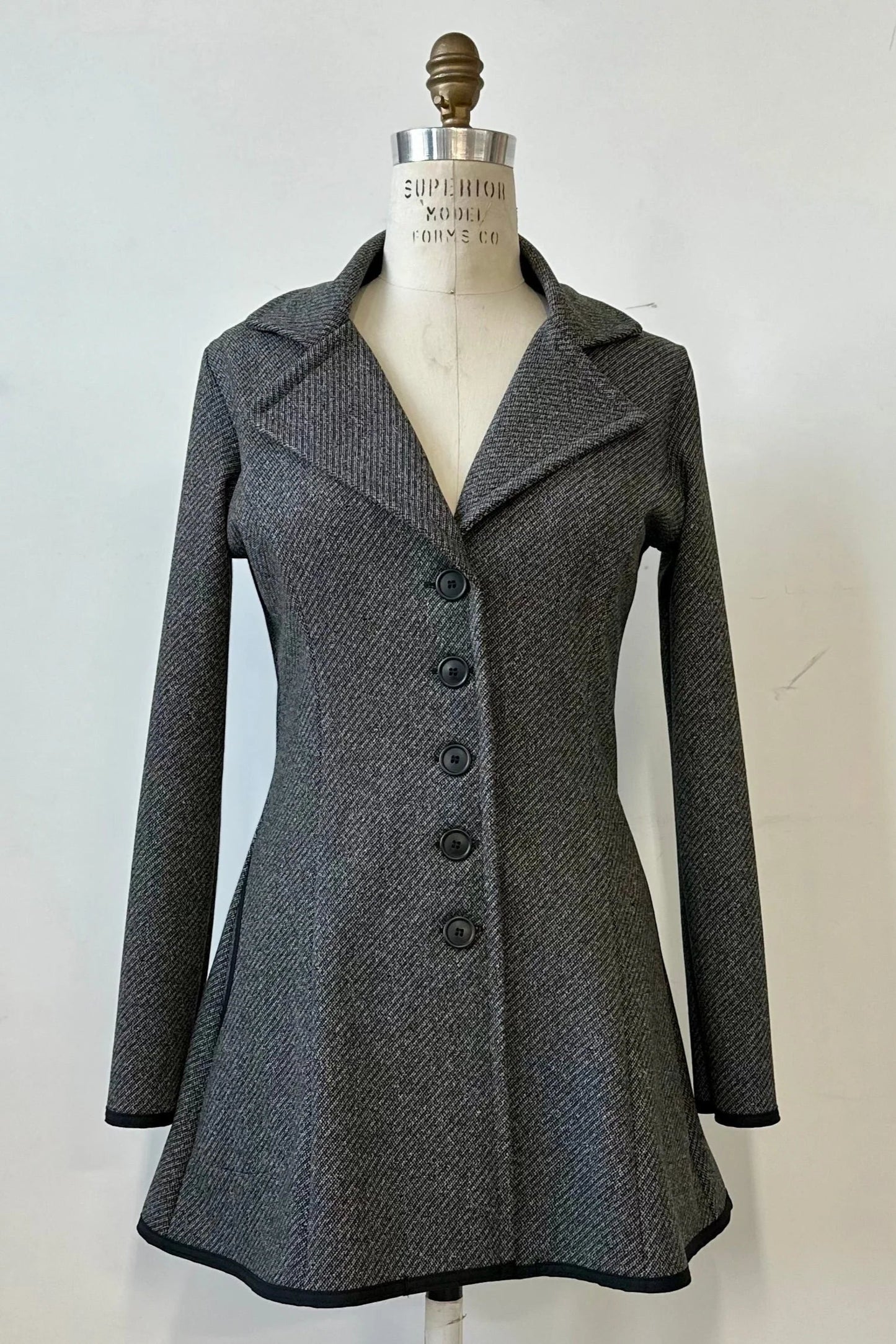 The Henderson Jacket by Kollontai in Charcoal tweed, with a fitted A-line shape that flares from the waist, a classic collar, and buttons down the front, shown on a mannequin in front of a white background. 