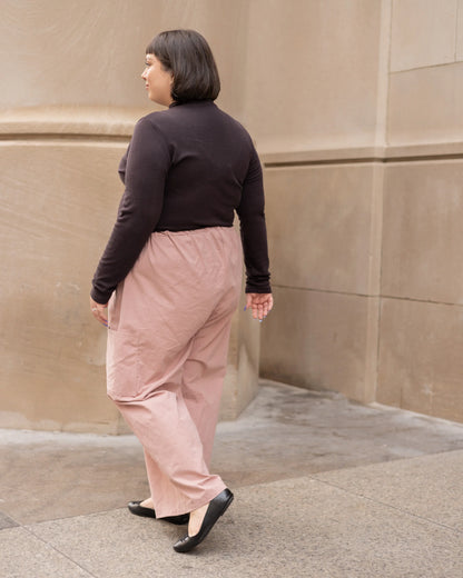 Side view of woman wearing the Essential Turtleneck by Lights of All in Coffee with brown pants, walking down the street.