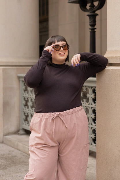 A woman wearing the Essential Turtleneck by Lights of All in Coffee with brown pants, standing on the street.