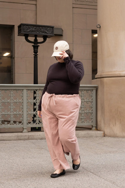 A woman wearing the Essential Turtleneck by Lights of All in Coffee with brown pants, standing on the street.