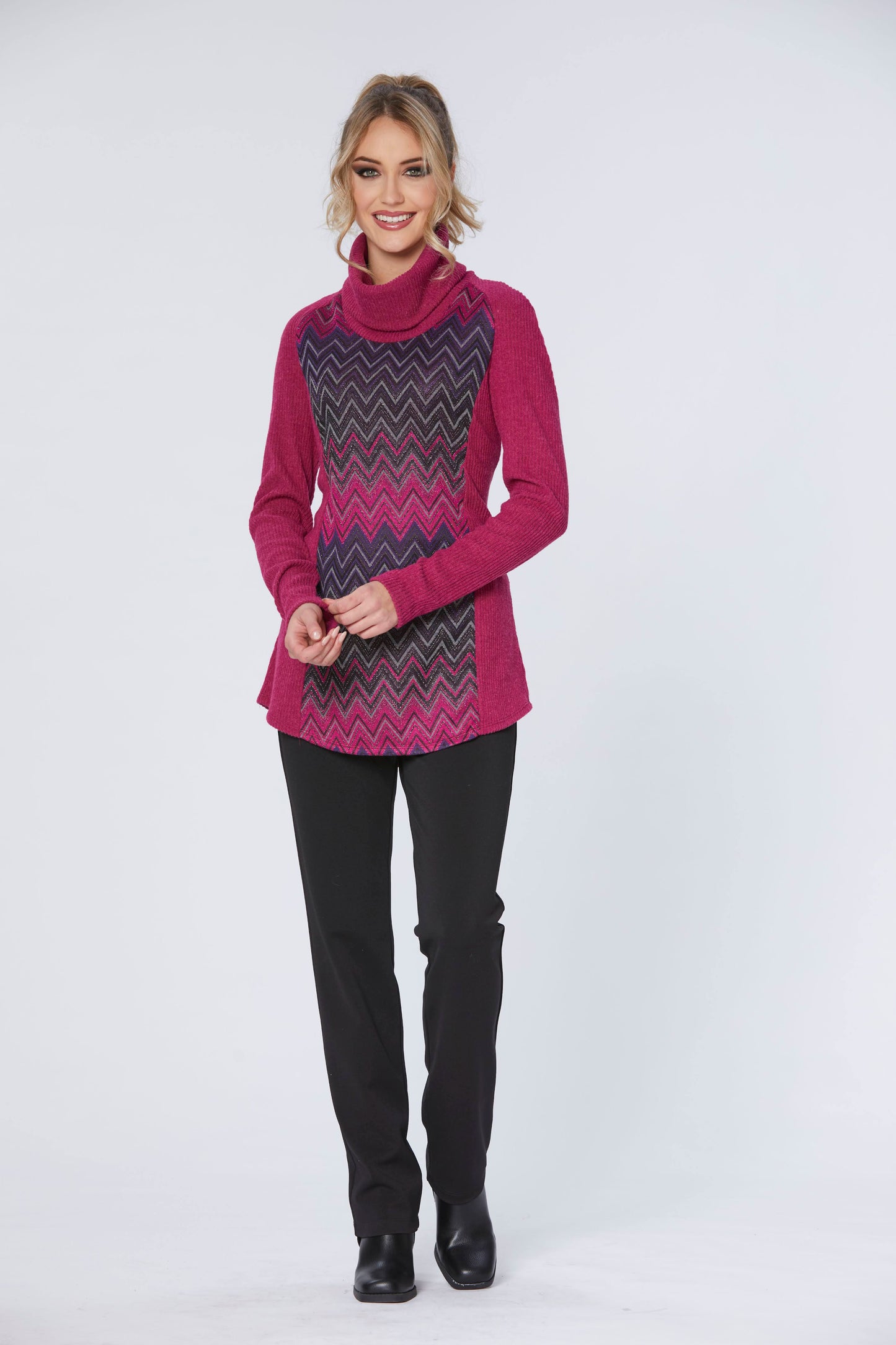 A woman wearing the Heidi Tunic by Luc Fontaine in Pink with black pants, standing in front of a white background 