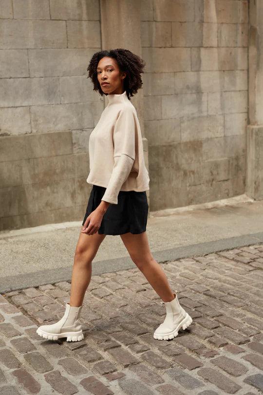 Side view of a woman wearing the Cali Short by MAS in Pepper with a beige top, standing on a cobblestone street