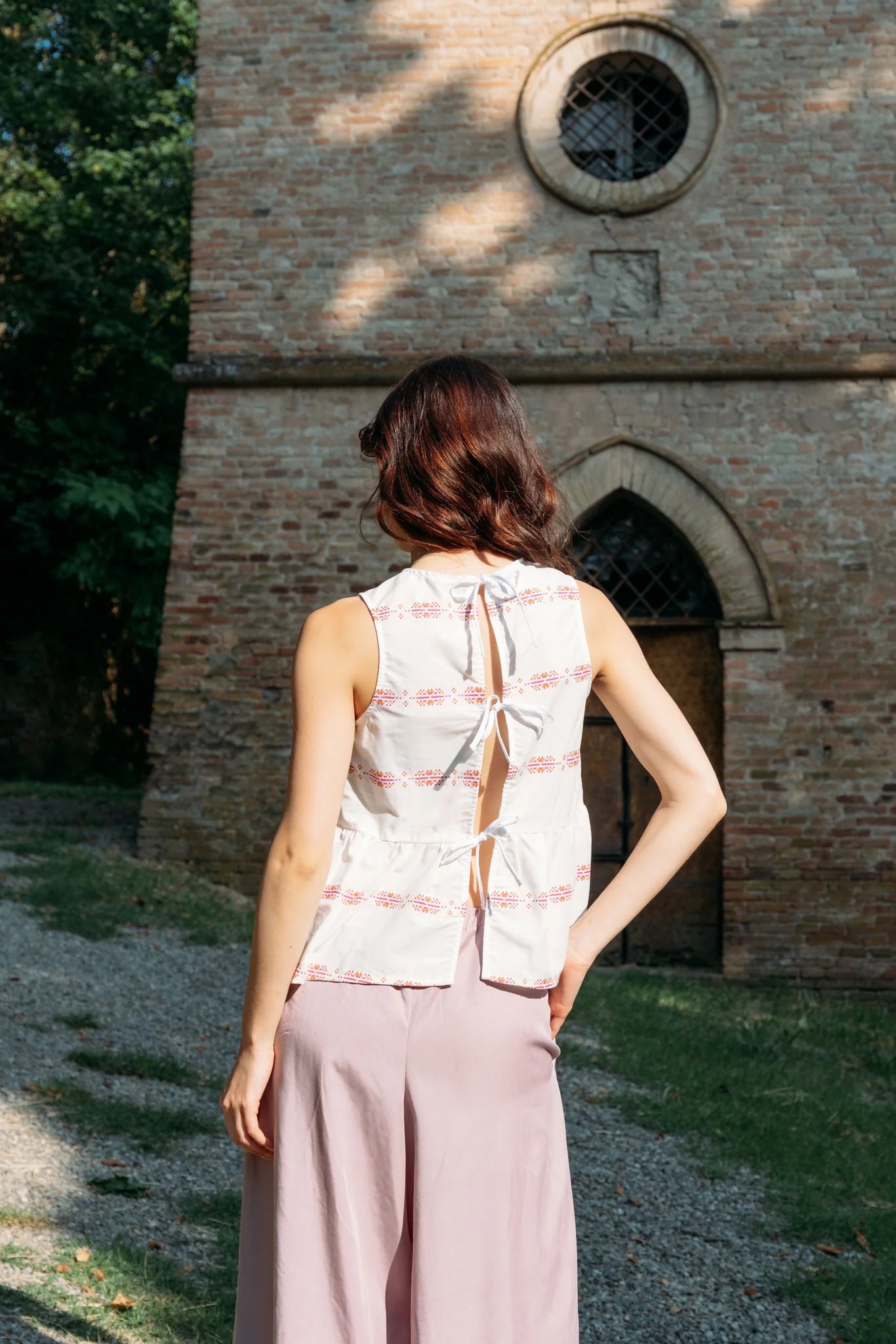 Back view of a woman wearing the Siena Pants by MAS in Raspberry, wide legged trousers with an elastic waist. She is wearing them with a white top and standing outdoors by a historic building. 