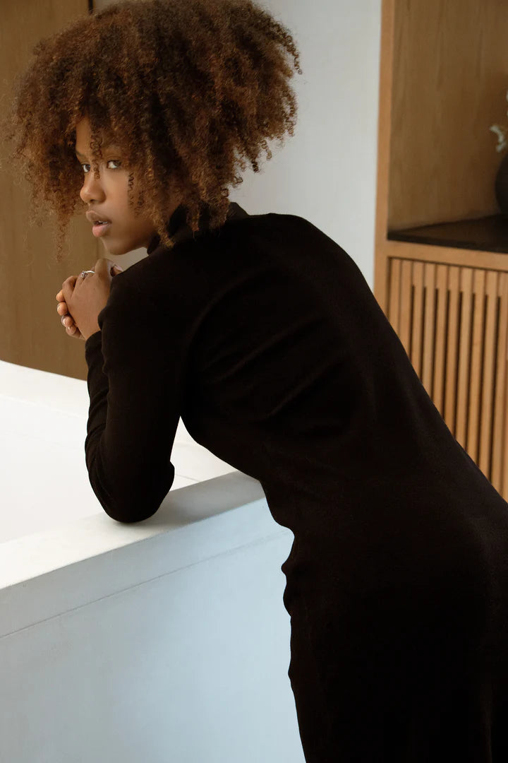 Back view of a woman wearing the MAS Mecca Dress in Pepper, leaning against a white counter